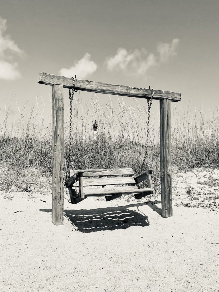 Holzschaukel für mehrere Personen mit Blick aufs Meer, im Hintergrund ein Leuchtturm